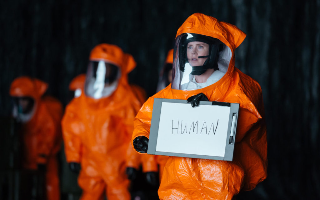 Imagem com a atriz do filme A Chegada com um quadro onde está escrito 'Human'